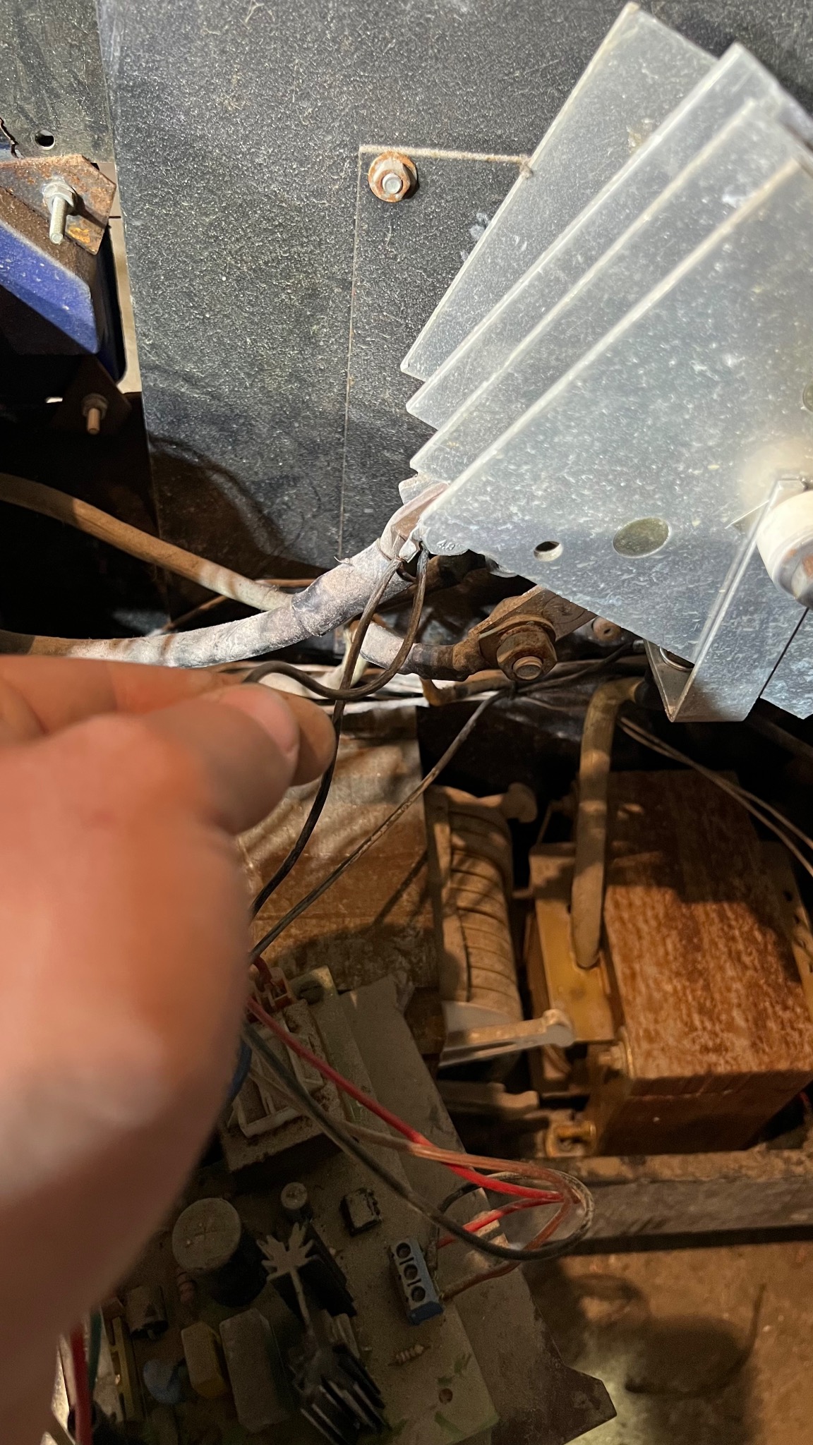 Wnętrze starego, zakurzonego urządzenia elektrycznego z widocznymi przewodami, płytką drukowaną i radiatorem, palec wskazujący na jeden z przewodów.