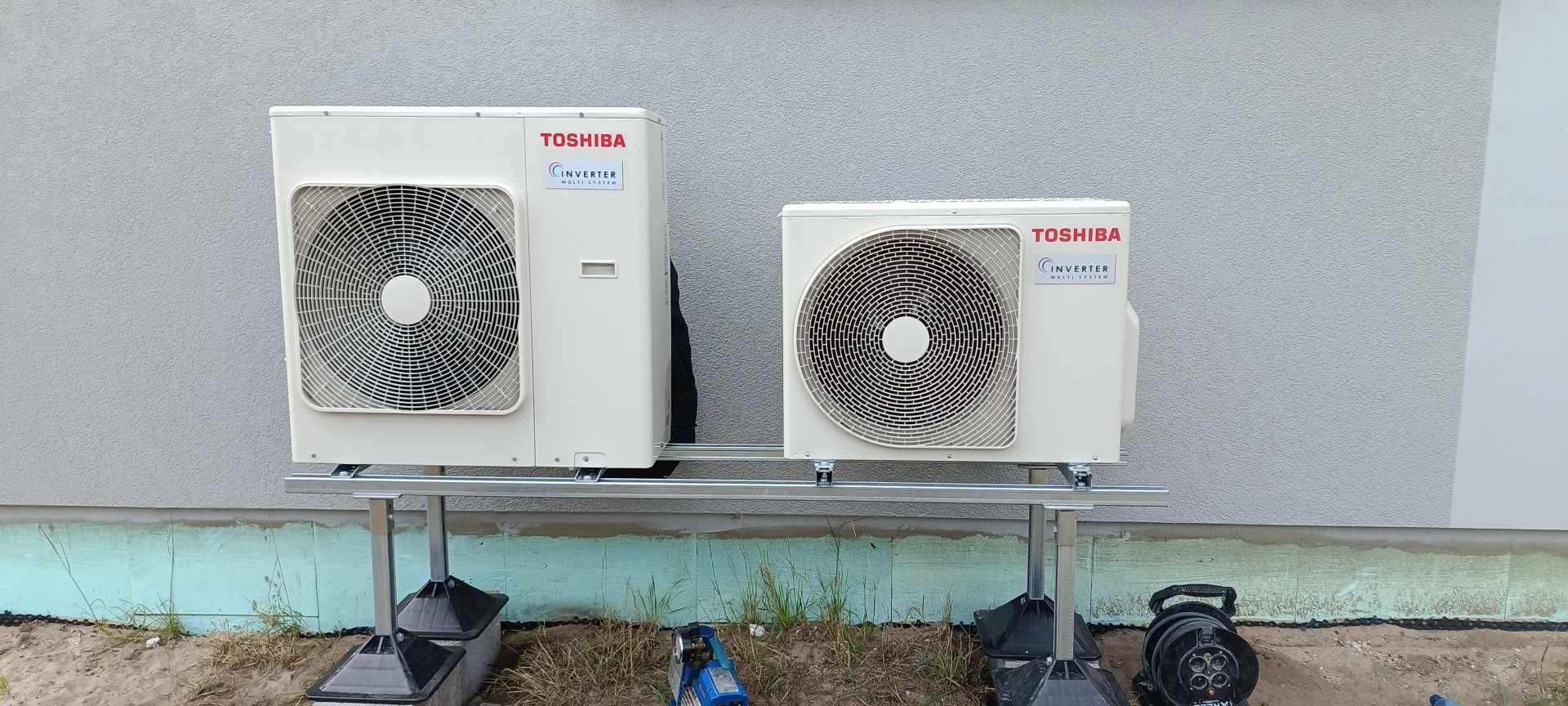 Dwie jednostki zewnętrzne klimatyzacji Toshiba Inverter Multisystem zamontowane na aluminiowej konstrukcji przy ścianie budynku z ociepleniem fundamentów.