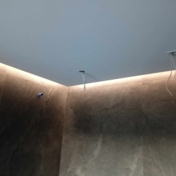 Mika'EL - Wnętrze łazienki z podświetleniem LED wzdłuż sufitu, widoczne przewody wystające z sufitu przygotowane do montażu oświetlenia punktowego.