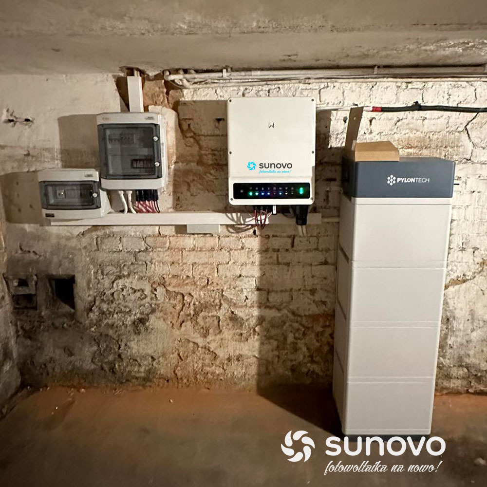 Instalacja domowa: akumulator Pylontech, inwerter Sunovo z diodami LED i skrzynki elektryczne na tle ściany z cegły z widocznymi śladami wilgoci.