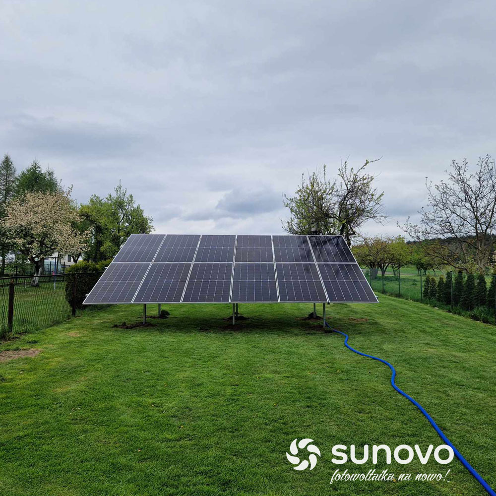 Instalacja fotowoltaiczna Sunovo na trawniku, widoczny niebieski kabel i ogrodzenie w tle.