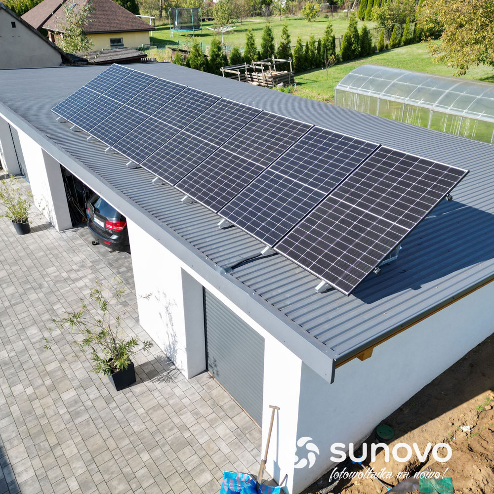 Panele słoneczne na dachu garażu z blachy trapezowej, widok z góry, na podjeździe kostka brukowa i zaparkowany samochód.
