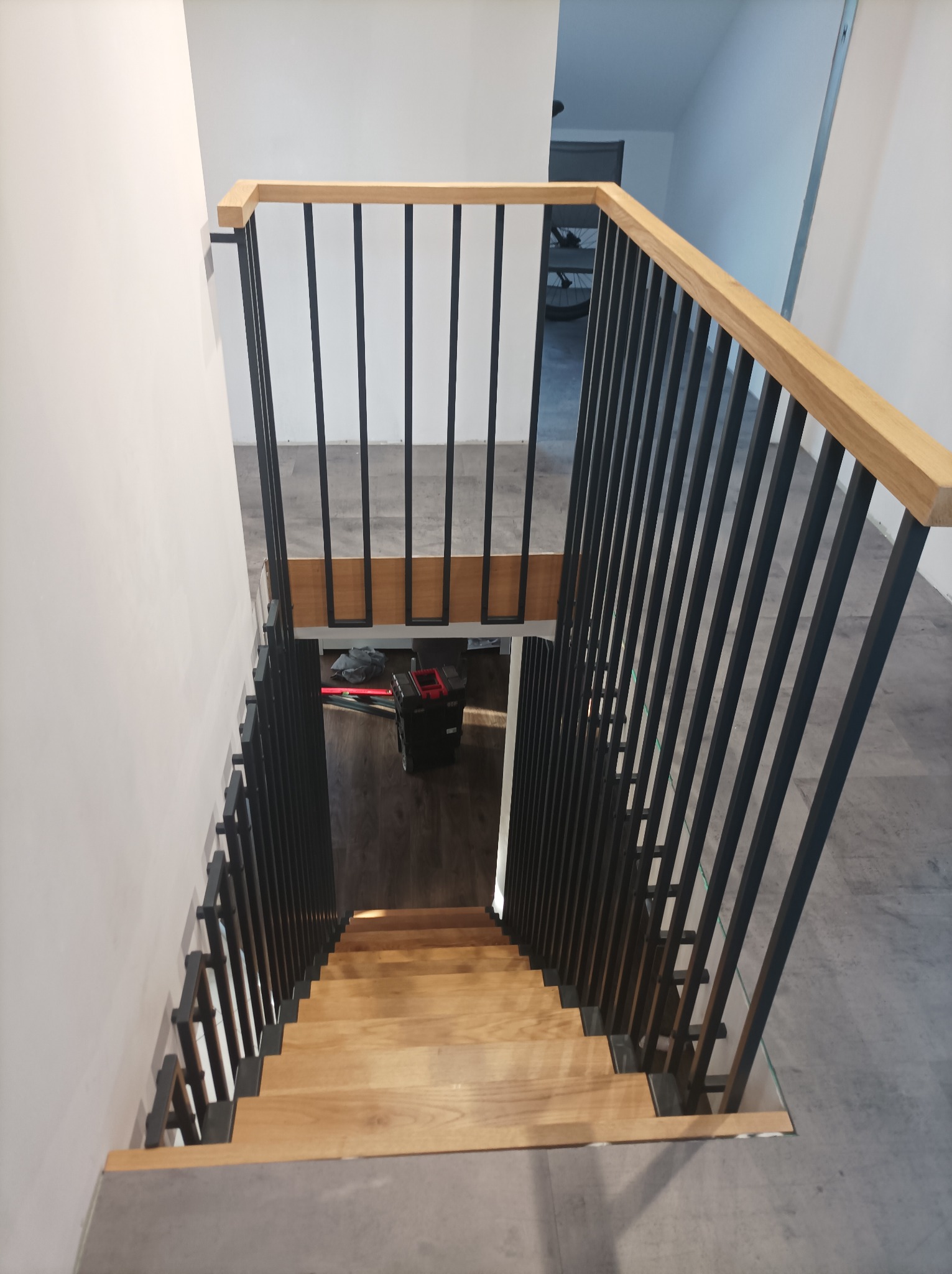 Nowoczesne schody drewniane z czarną, metalową balustradą widziane z góry, z narzędziami budowlanymi w tle.