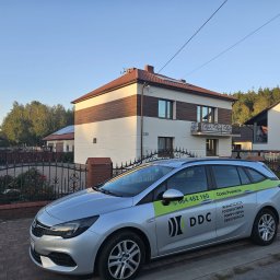 DDC Arkadiusz Obszyński - Dom z panelami słonecznymi na dachu, na pierwszym planie srebrny samochód z logo firmy oferującej klimatyzację, fotowoltaikę, pompy ciepła i rekuperację.