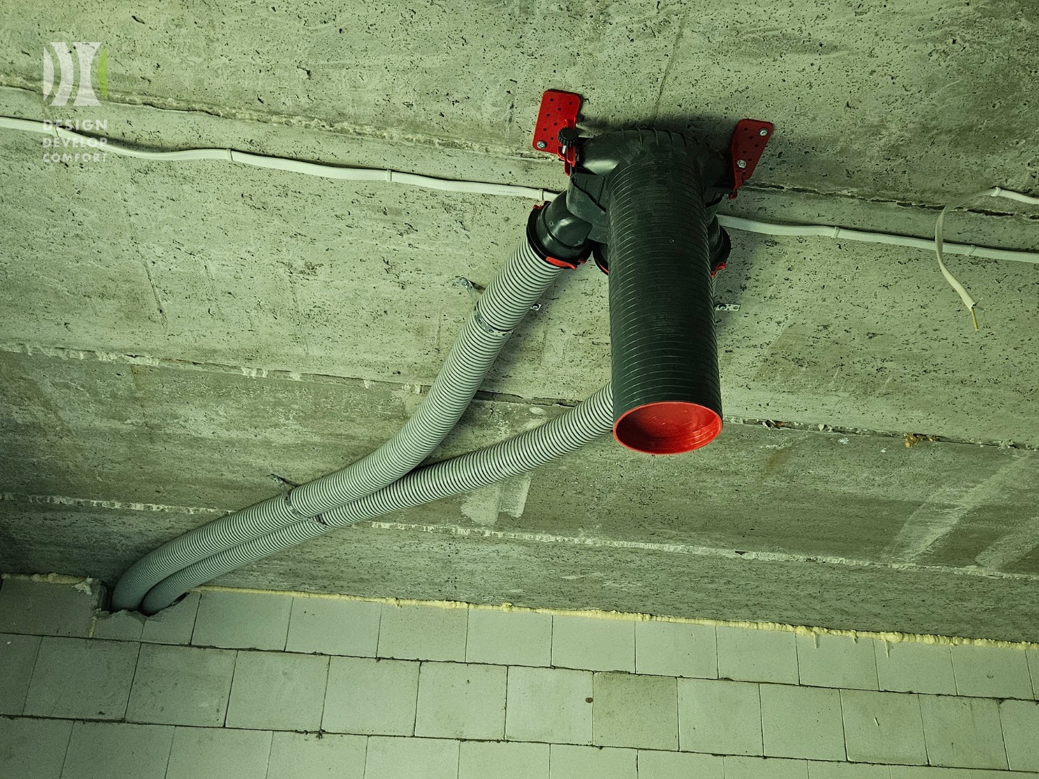 Szara instalacja wentylacyjna z dwoma elastycznymi przewodami przymocowana do sufitu z betonu komórkowego, widok z dołu.