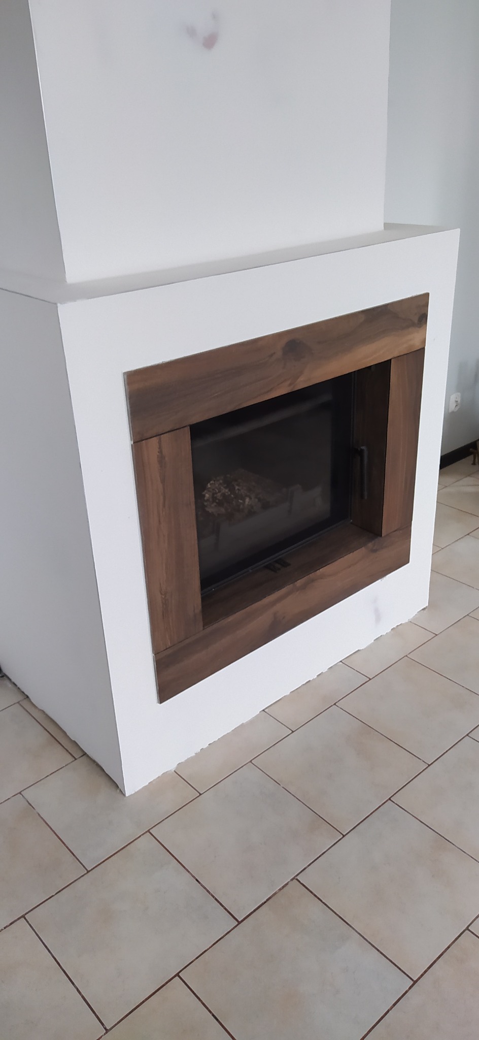 Nowoczesny kominek obudowany białą konstrukcją z drewnianą ramą, widoczna część podłogi wyłożona płytkami.