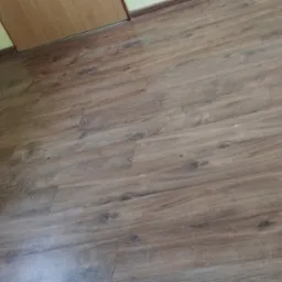 Ukończona podłoga z paneli o wzorze drewna, listwy przypodłogowe przy ścianie w kolorze kremowym, widoczny fragment drzwi.