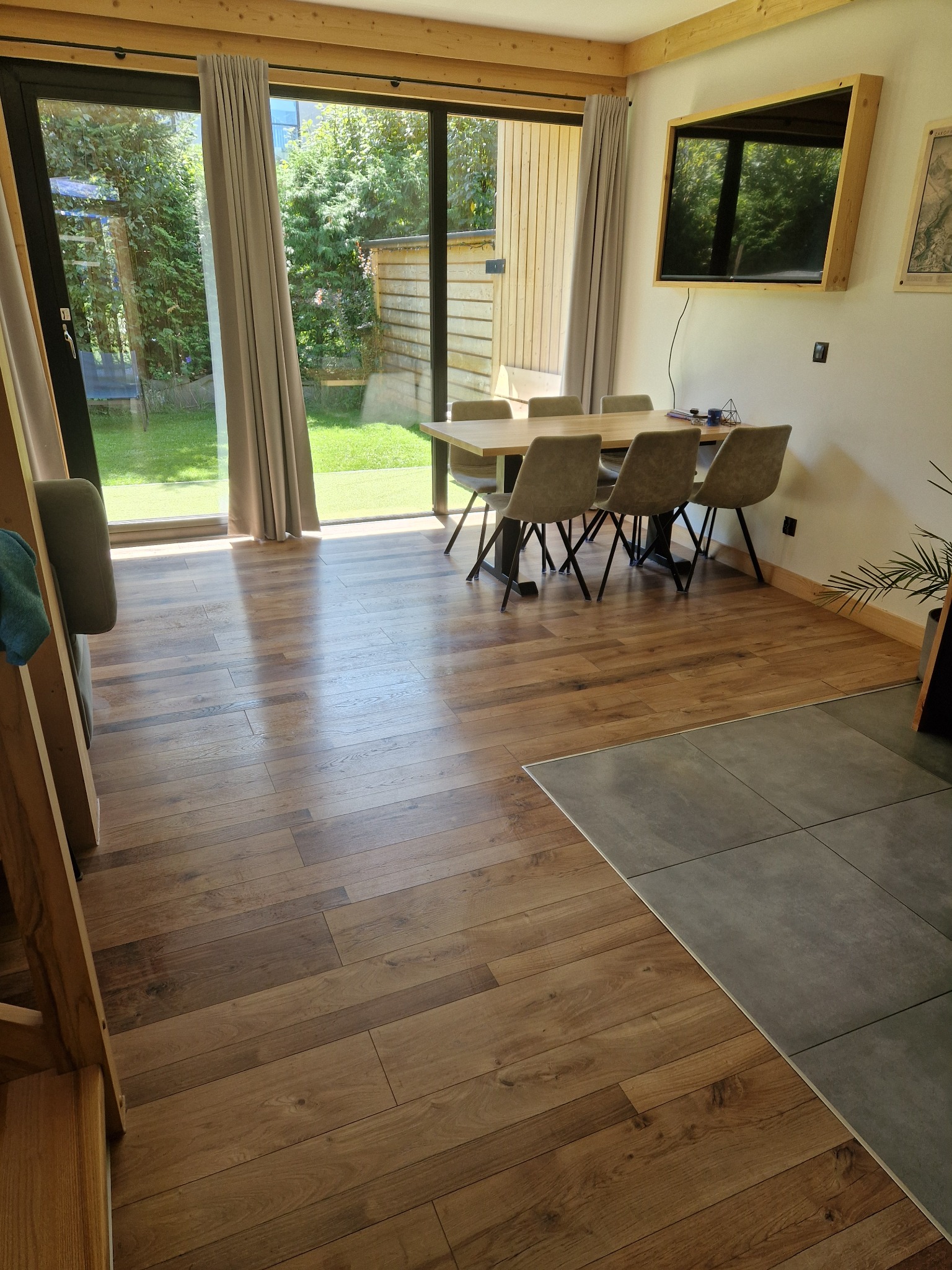 Jasne wnętrze domu z drewnianą podłogą, stołem jadalnym i widokiem na ogród przez duże okno.