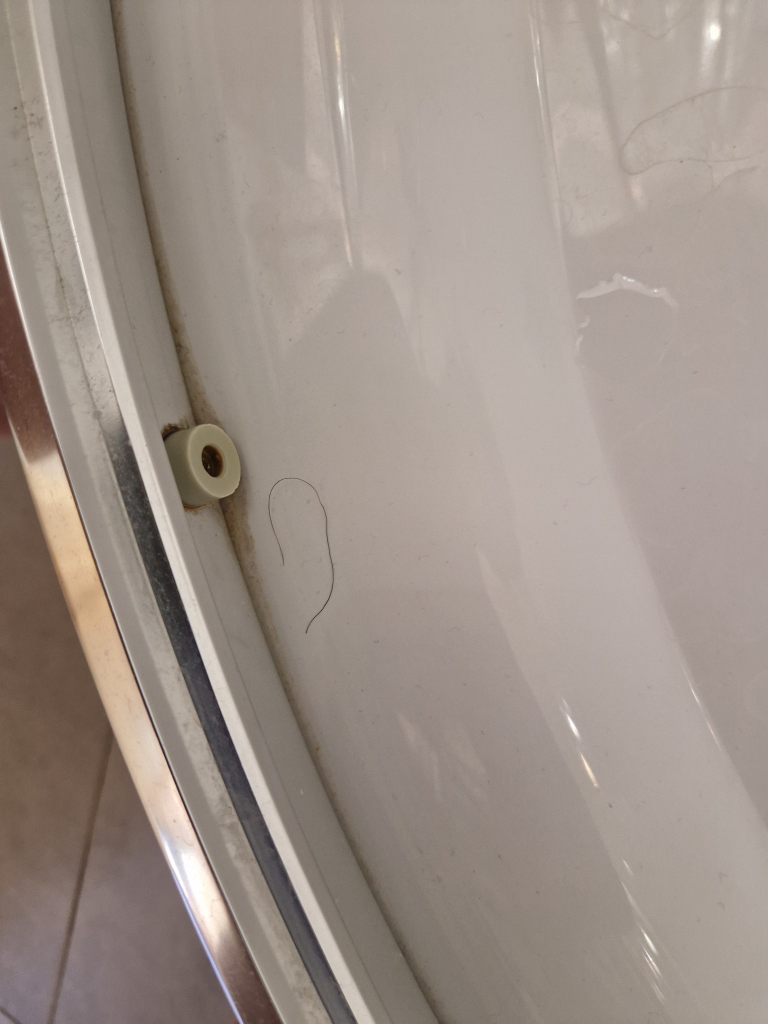 Brudna, biała rama okienna z pojedynczym włosem i plastikowym elementem mocującym. Widoczne ślady kurzu i zabrudzeń.