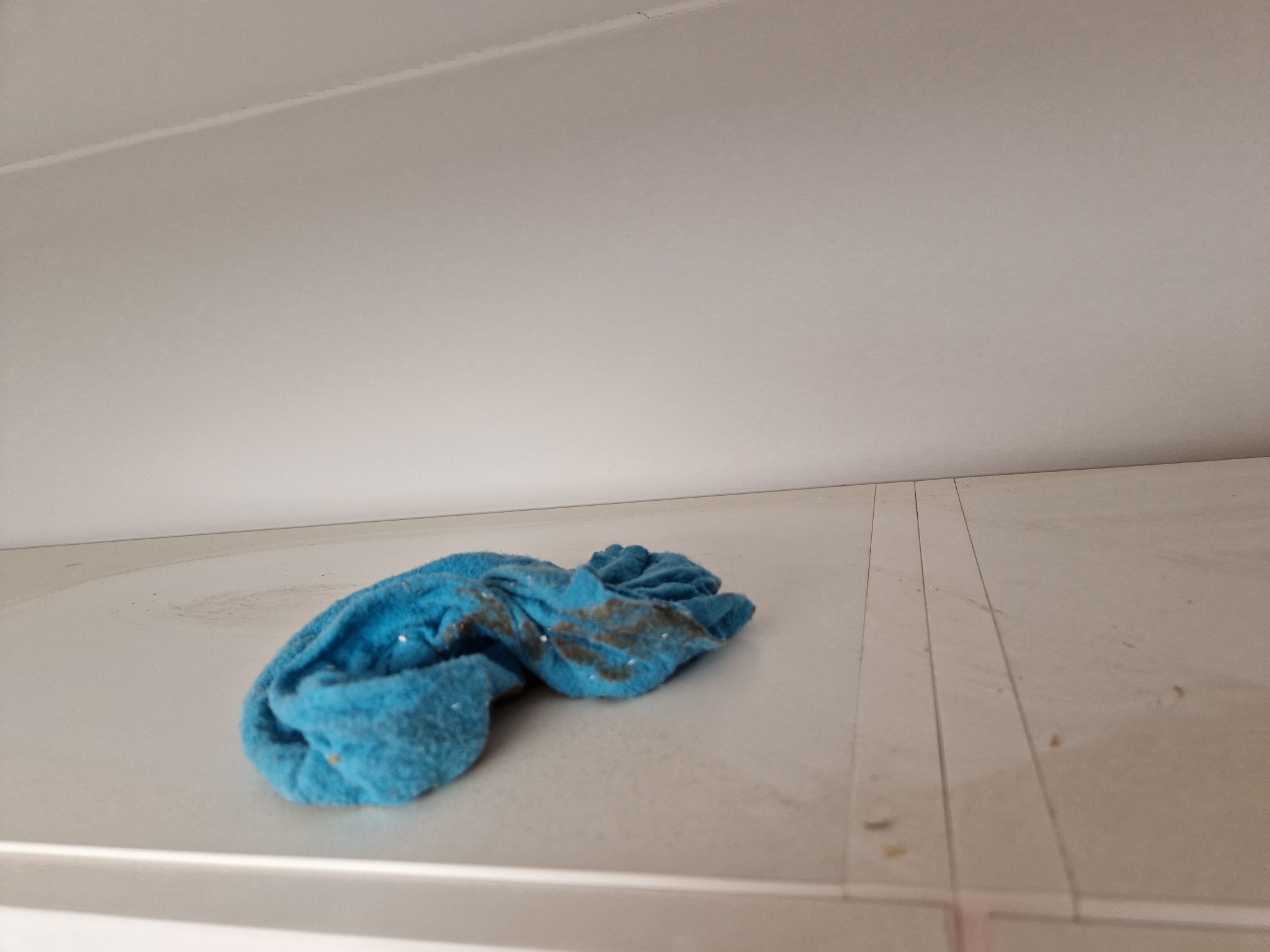 Brudna, zwinięta niebieska ścierka leży na białej, zabrudzonej powierzchni mebla lub podłogi; widoczne smugi i drobne zabrudzenia.