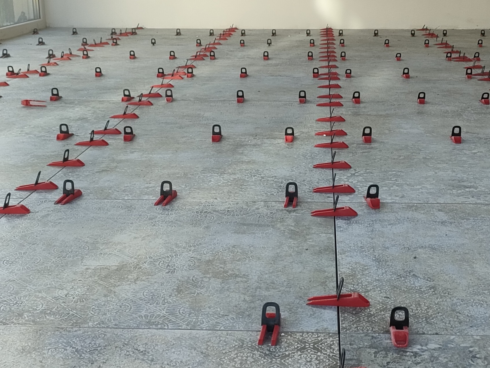 Ułożone płytki podłogowe z systemem poziomowania w postaci czerwonych klipsów i klinów, widok z góry, wzorzysta powierzchnia płytek.