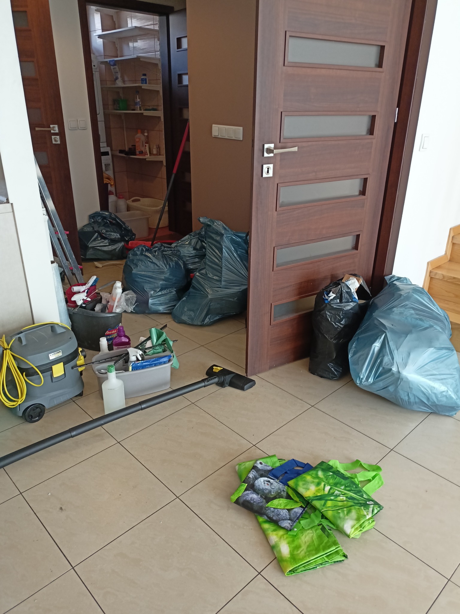 Pobojowisko po najemcy: worki na śmieci, sprzęt do sprzątania, odkurzacz przemysłowy i torby na podłodze w mieszkaniu po intensywnym sprzątaniu.