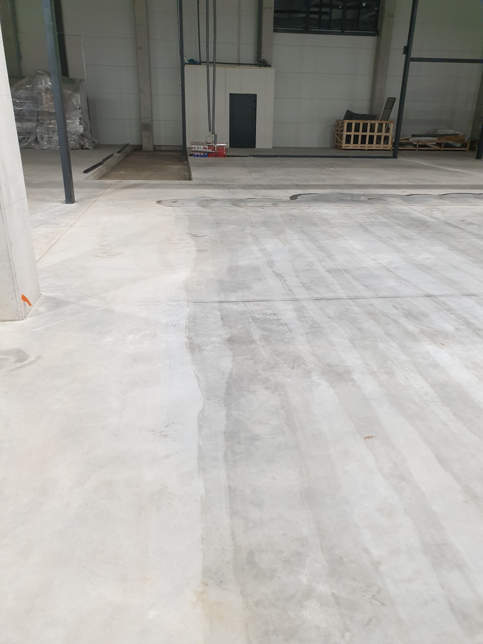 Betonowa posadzka w hali przemysłowej z widocznymi śladami czyszczenia, w tle regały i instalacje.