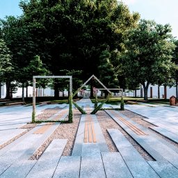 Flora Garden Mateusz Kołodziej - Nowoczesna aranżacja przestrzeni parkowej z geometrycznymi konstrukcjami porośniętymi zielenią, drewnianymi ławkami i równo przystrzyżonymi drzewami w tle.