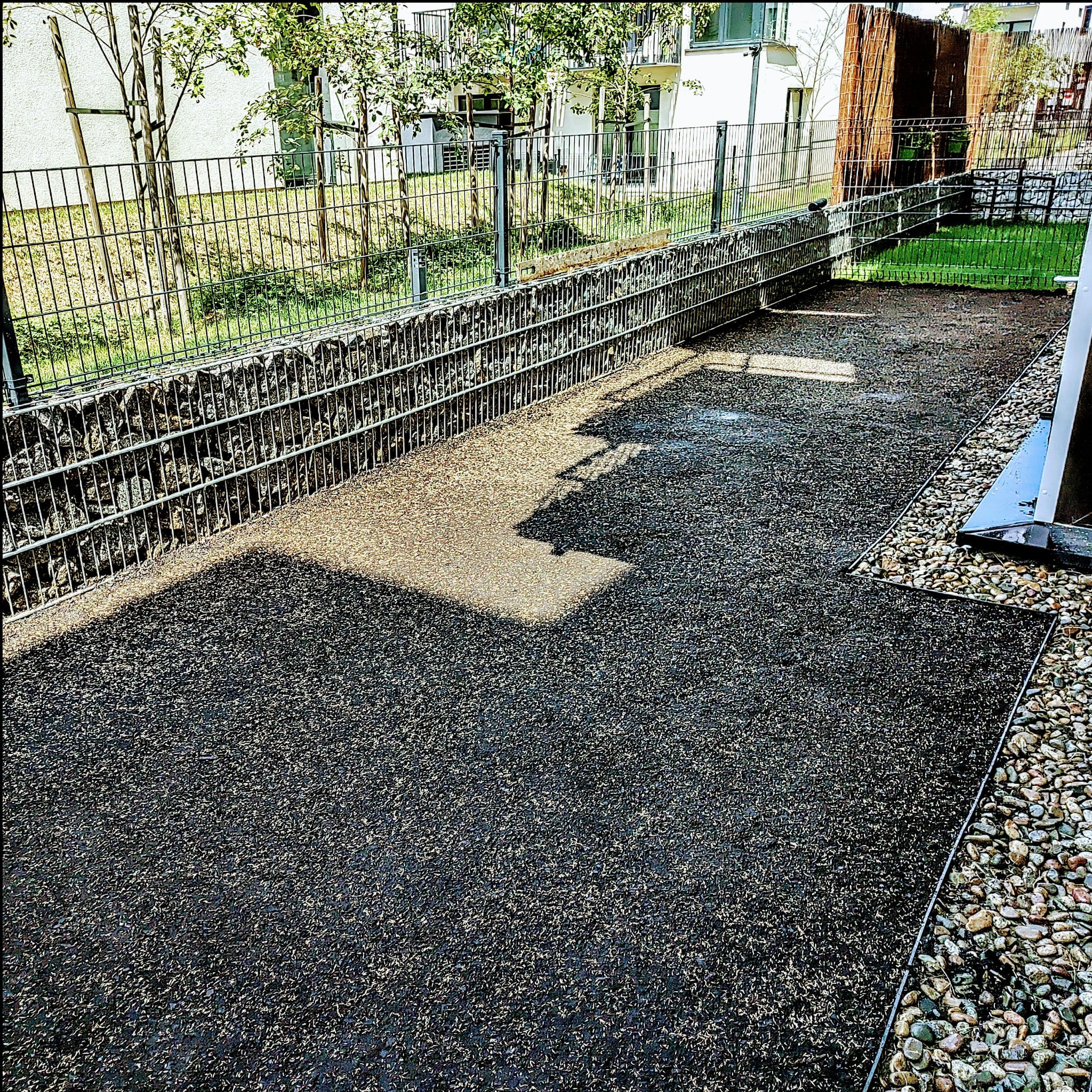 Przygotowany teren pod trawnik z rolki, widoczna siatka gabionowa w tle i kamienny obrzeże.