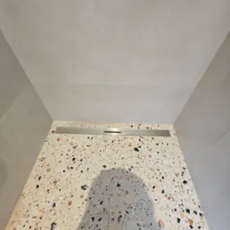 Wykończony brodzik w kabinie prysznicowej z odpływem liniowym i mozaiką lastryko na ścianie, widok z góry w dół.