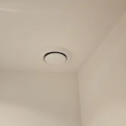Biały, okrągły nawiewnik sufitowy z czarnym wnętrzem, zamontowany w rogu pomieszczenia o jasnych ścianach.