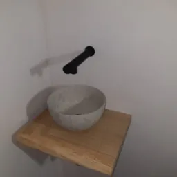 Umywalka nablatowa w kolorze terrazzo na drewnianym blacie, z czarną baterią ścienną w minimalistycznej łazience.