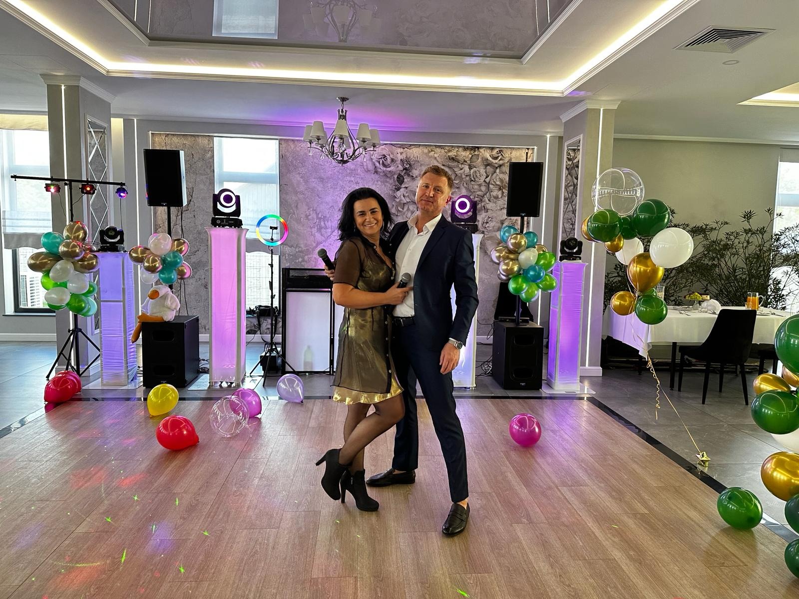 Duet konferansjerów z mikrofonami na tle sali z dekoracjami balonowymi i oświetleniem eventowym, Wieliczka. Scena gotowa na imprezę.