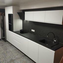 EMa - Miłosz Zadka - Nowoczesna kuchnia z białymi szafkami i czarnym blatem, minimalistyczny design, czarny panel nad blatem, widok na zlew i płytę grzewczą.
