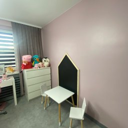 EMa - Miłosz Zadka - Pokój dziecięcy po odświeżeniu: ściany w odcieniach różu, białe meble dziecięce, zabawki na komodzie. Minimalistyczny design, jasne wnętrze.