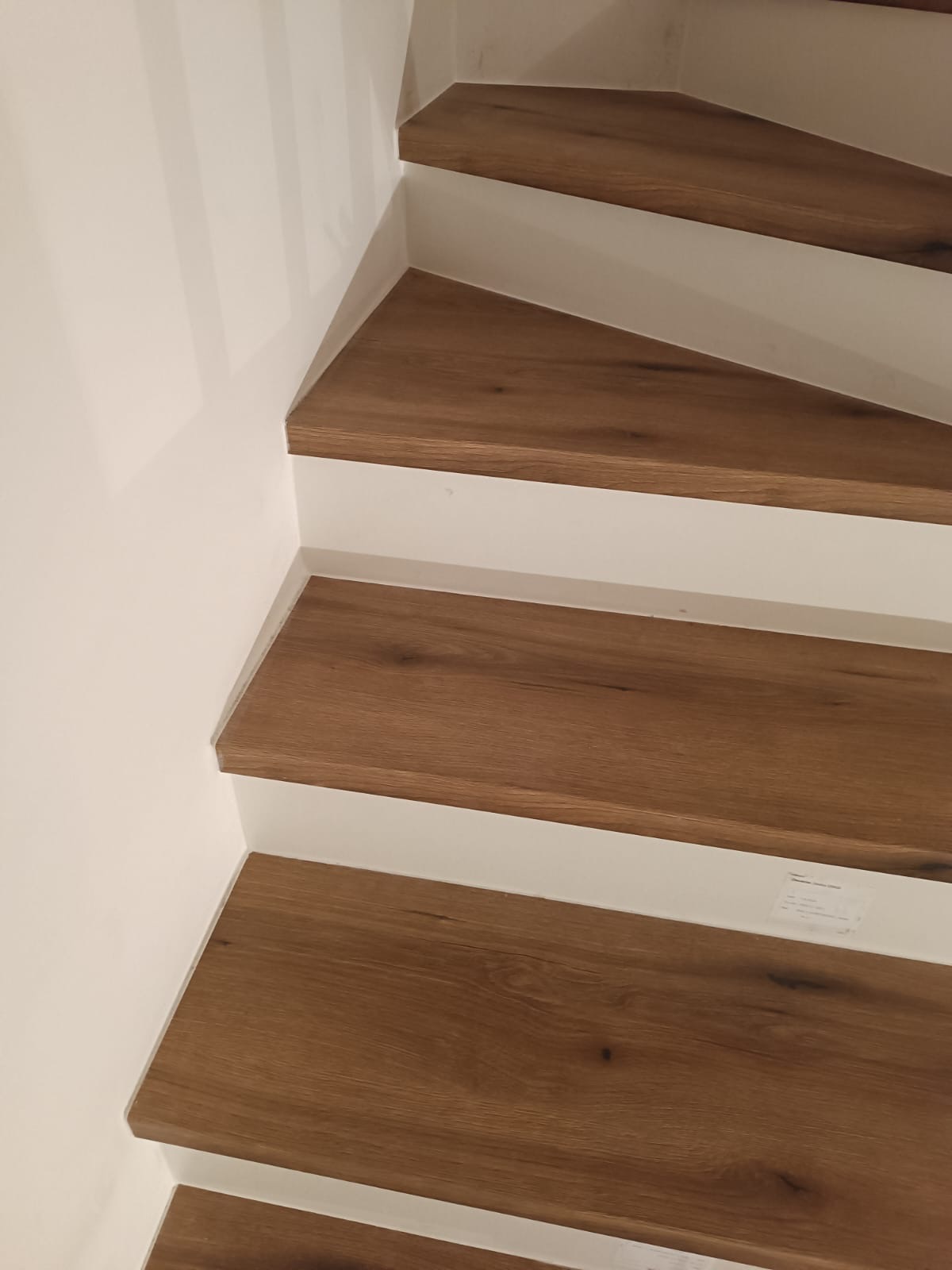 Drewniane stopnie schodów z białymi podstopnicami, widoczne z bliska, z delikatnym oświetleniem podkreślającym strukturę drewna i czystość wykonania.