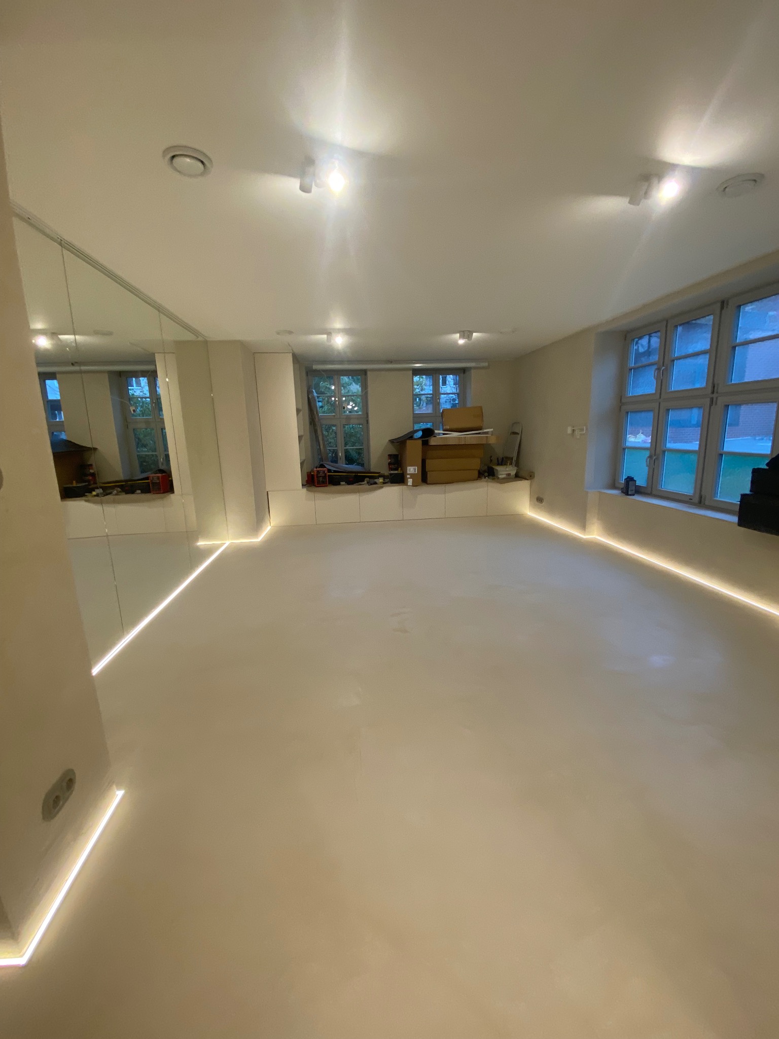 Jasne, przestronne wnętrze po remoncie z podświetleniem LED wzdłuż podłogi i lustrem na ścianie. Widoczne okna i minimalistyczne wykończenie.