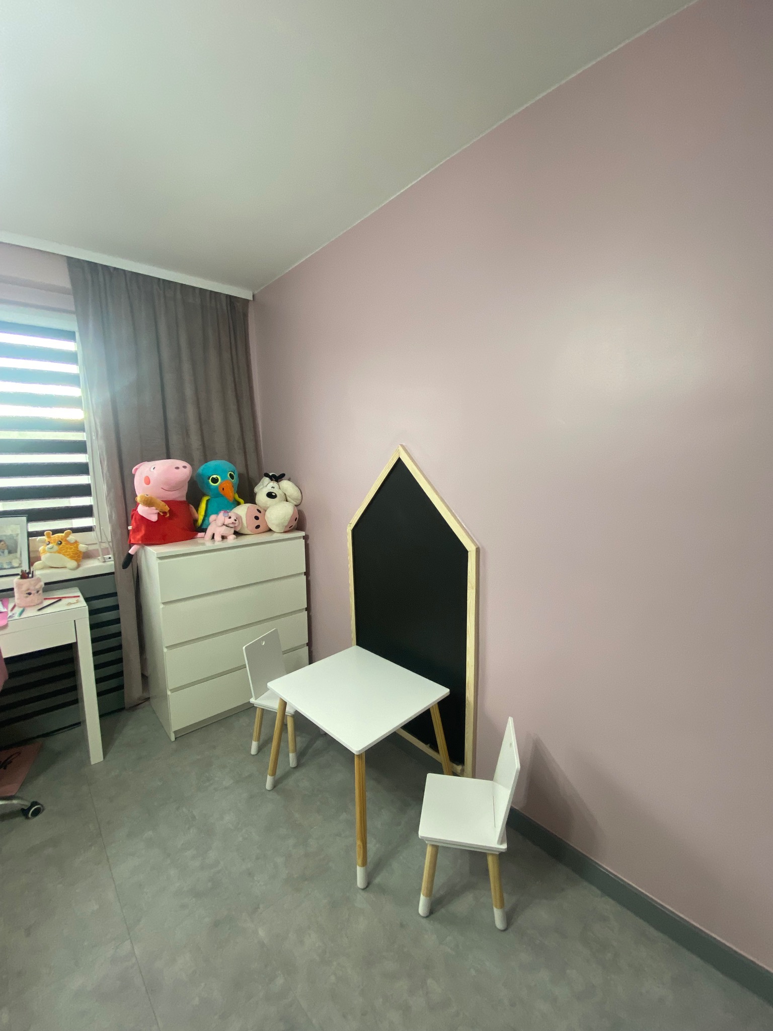 Pokój dziecięcy po odświeżeniu: ściany w odcieniach różu, białe meble dziecięce, zabawki na komodzie. Minimalistyczny design, jasne wnętrze.