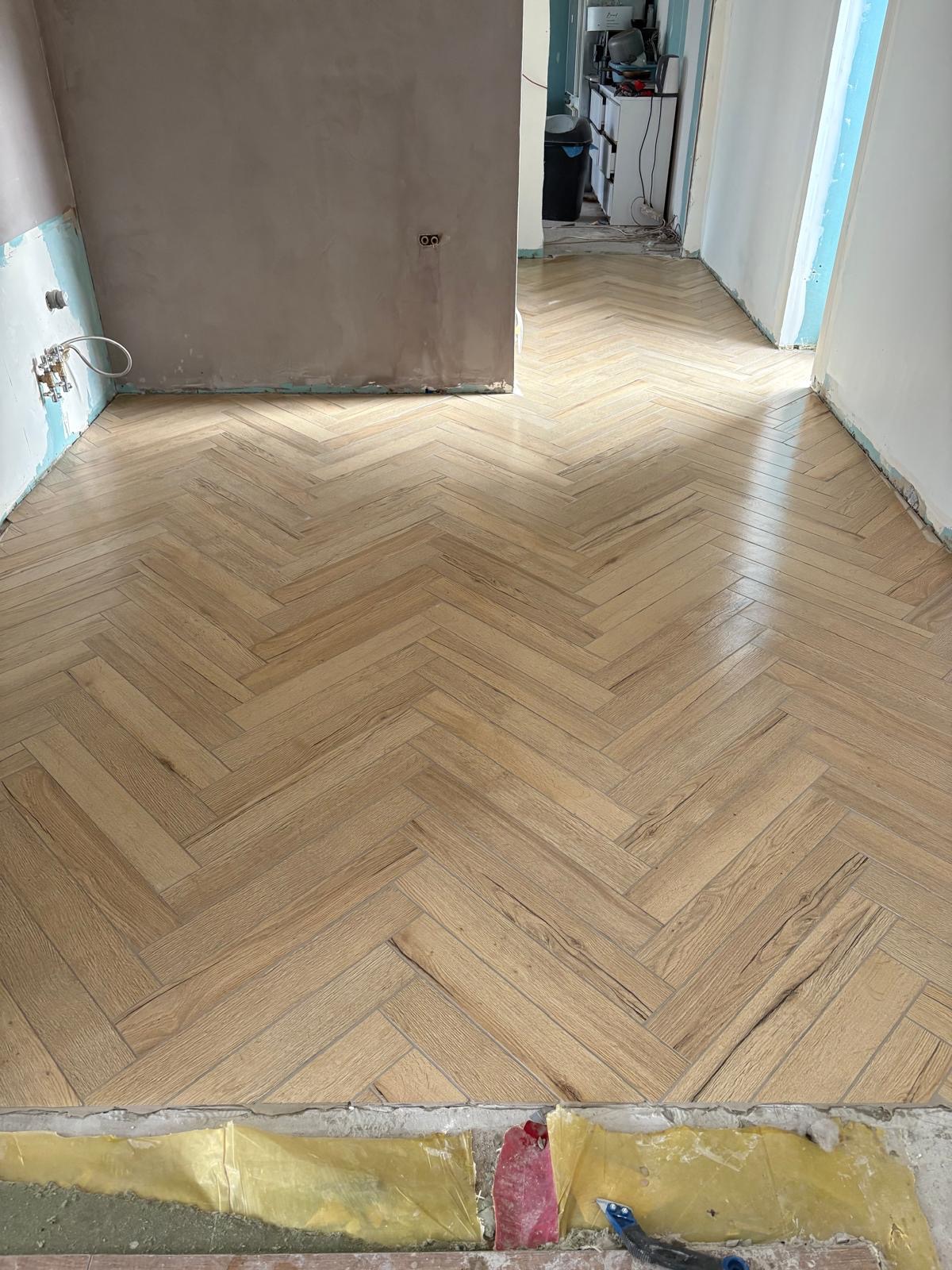 Ułożona, jasna podłoga z paneli w jodełkę w trakcie remontu mieszkania. Widoczne przygotowane ściany i fragment zabezpieczonej podłogi. Naturalne światło.