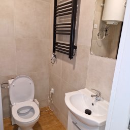 Pawex-bud - Nowoczesna, jasna łazienka z beżowymi płytkami, drewnopodobną podłogą, białym zlewem z szafką, wiszącym grzejnikiem drabinkowym i toaletą z otwartą klapą.