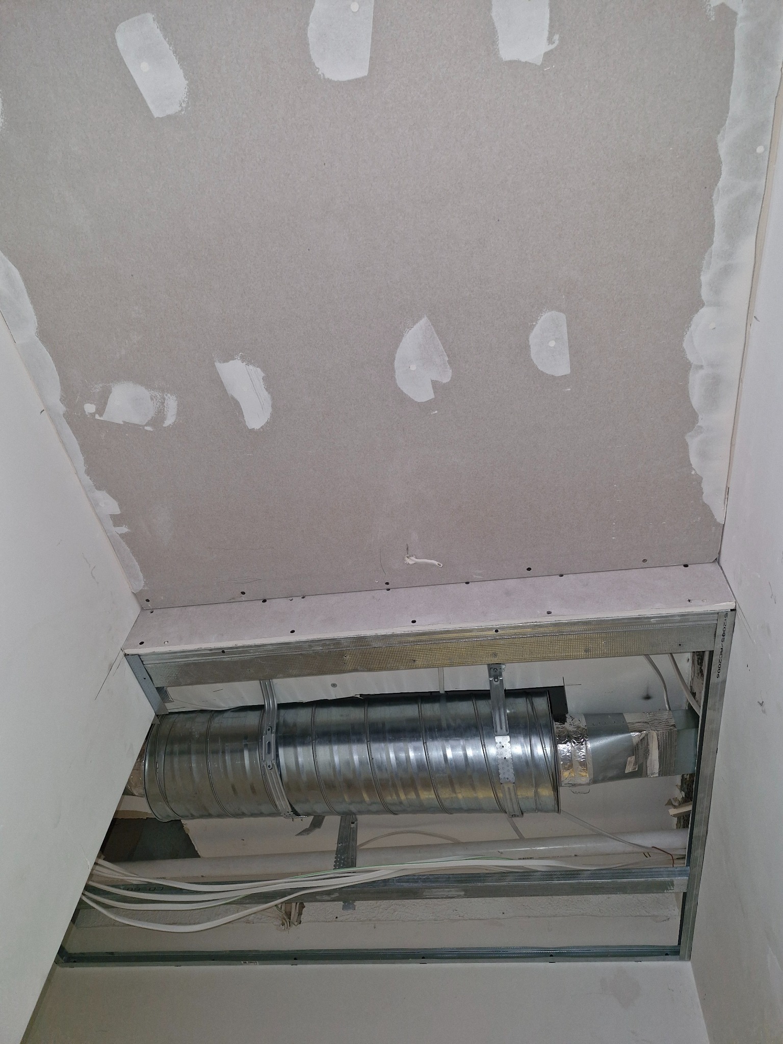 Sufit podwieszany w trakcie montażu z widoczną instalacją wentylacyjną, kable i płyty gipsowo-kartonowe z widocznymi miejscami szpachlowania.