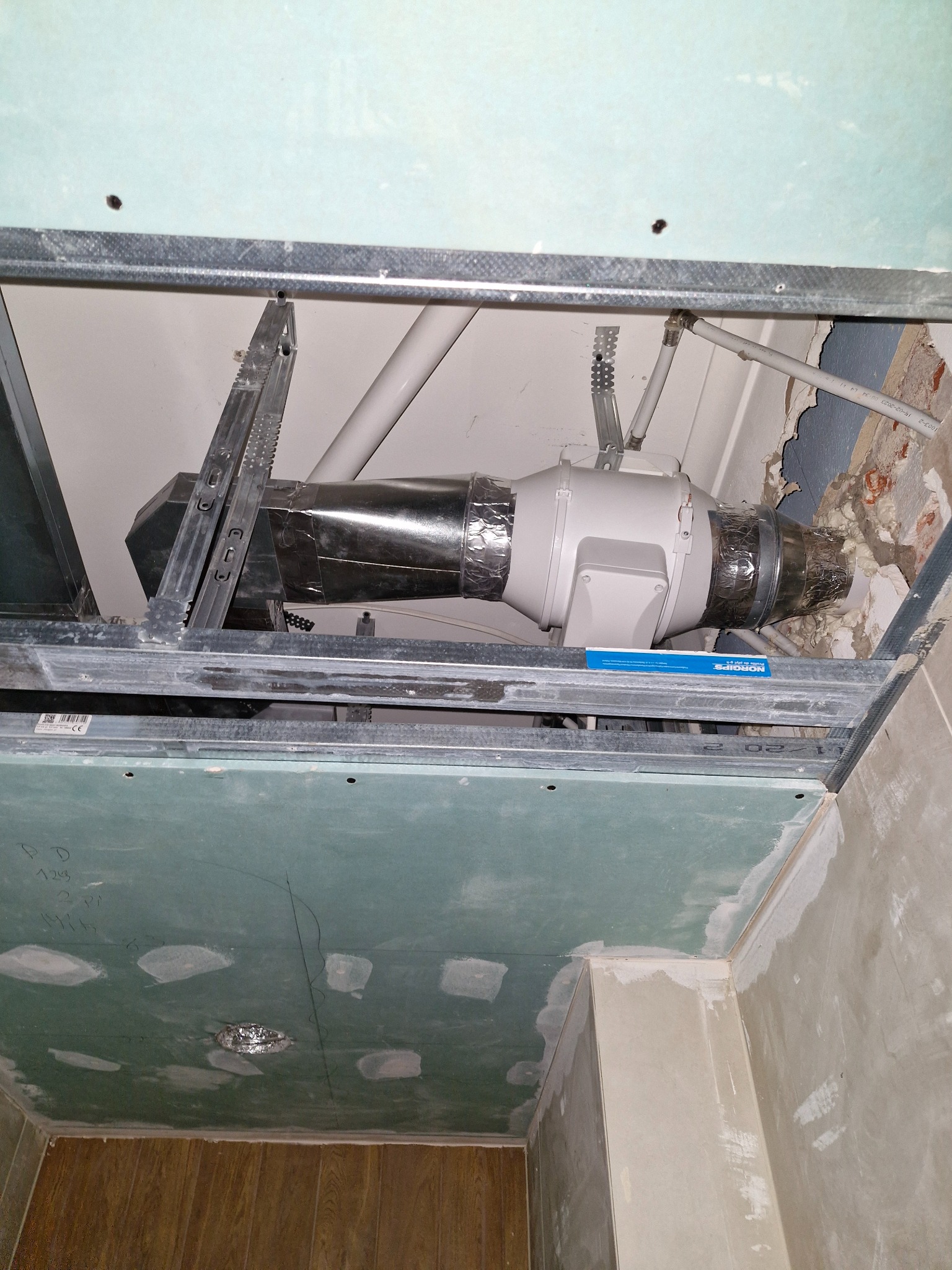 Montaż wentylacji sufitowej w pomieszczeniu w trakcie prac wykończeniowych, widoczne profile metalowe, płyta gipsowo-kartonowa, rury i wentylator kanałowy.