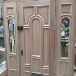 Surowe, drewniane drzwi wejściowe z szybkami bocznymi, widoczne detale wykończenia i okucia, w tle warsztat.