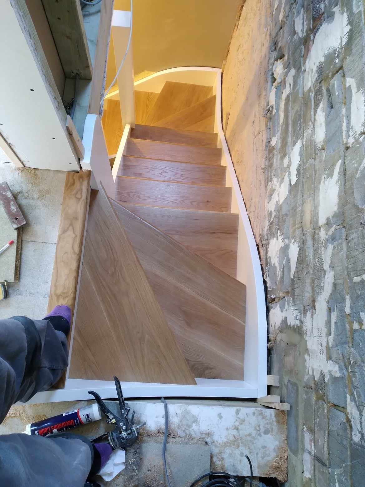 Montaż drewnianych schodów z białymi balustradami; widoczne narzędzia i częściowo wykończona ściana z surowego betonu.