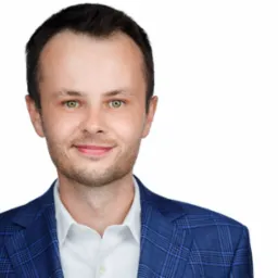 Portret uśmiechniętego mężczyzny w niebieskiej marynarce w kratę i białej koszuli na białym tle.