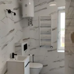Nowoczesna łazienka z marmurowymi płytkami, białymi meblami, grzejnikiem drabinkowym i podgrzewaczem wody.