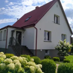 Jasna elewacja domu jednorodzinnego z czerwonym dachem, numerem 11 i bujnymi hortensjami w ogrodzie, widok z poziomu ogrodu w słoneczny dzień.