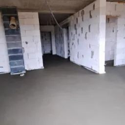 Wylana, świeża wylewka w surowym stanie, widoczne ściany z białego bloczka, instalacje pod sufitem.