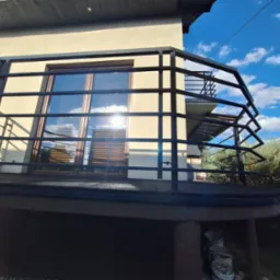 Nowoczesna, czarna balustrada balkonowa z metalu, widok z dołu, z refleksami słońca na oknach. Minimalistyczny design i błękitne niebo w tle.