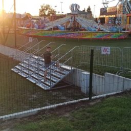 Weldcut spawanie i cięcie s.c. - Metalowe schody z poręczami prowadzące do podziemnego pomieszczenia na tle wesołego miasteczka w promieniach zachodzącego słońca.