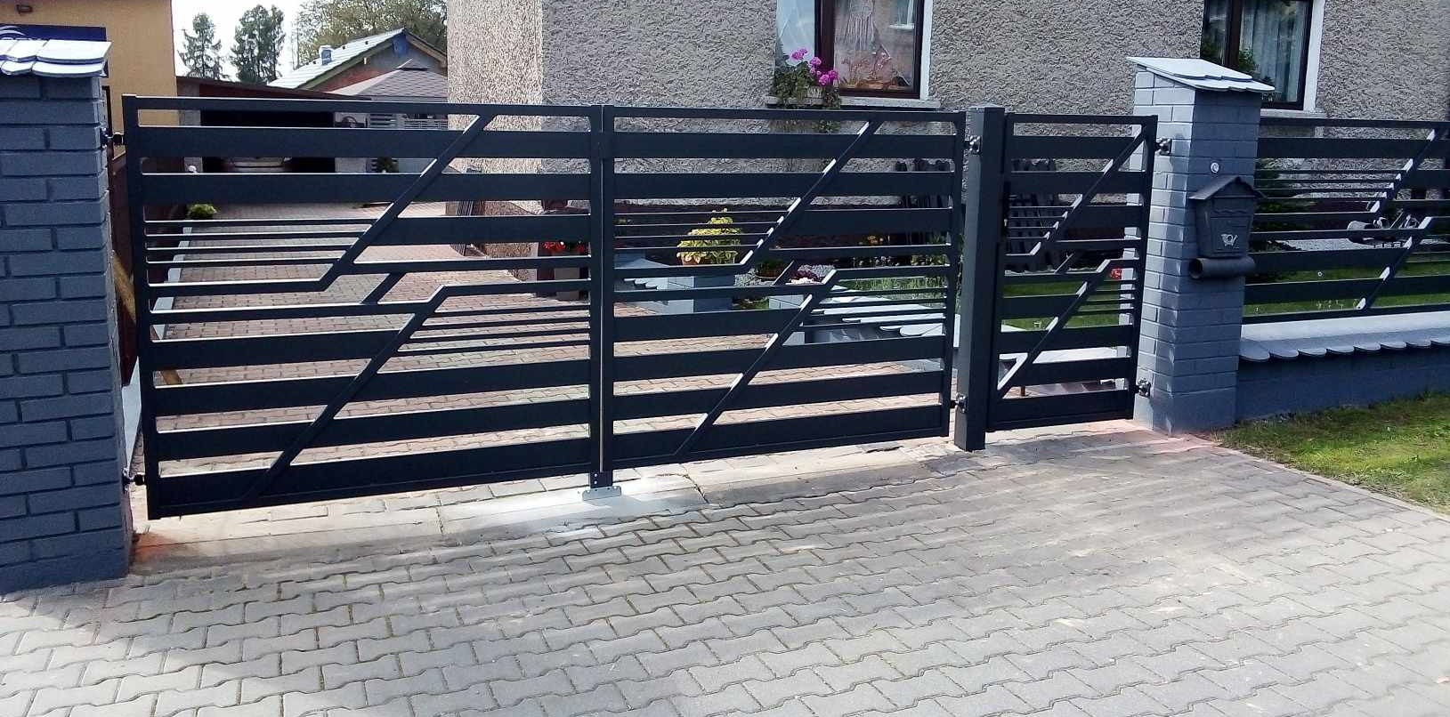 Nowoczesna, czarna brama wjazdowa z poziomymi profilami i geometrycznym wzorem, zamontowana na posesji z brukowaną nawierzchnią i murowanym słupkiem z skrzynką pocztową.