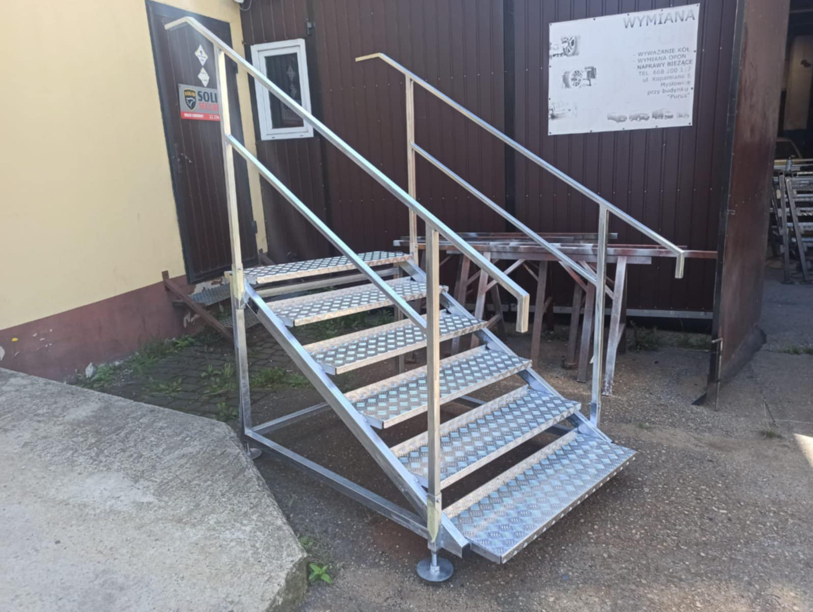 Zewnętrzne schody metalowe z poręczami, z antypoślizgowymi stopniami. Konstrukcja ustawiona na regulowanych stopach, widok z dołu.