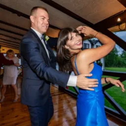 Uśmiechnięta para w tańcu podczas uroczystości weselnej w drewnianej altanie z widokiem na ogród.