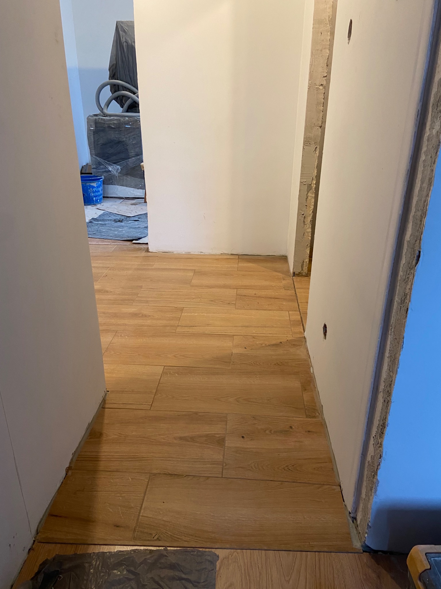 Układanie paneli podłogowych imitujących drewno w trakcie remontu łazienki, widoczne niedokończone ściany i przygotowane materiały w tle.