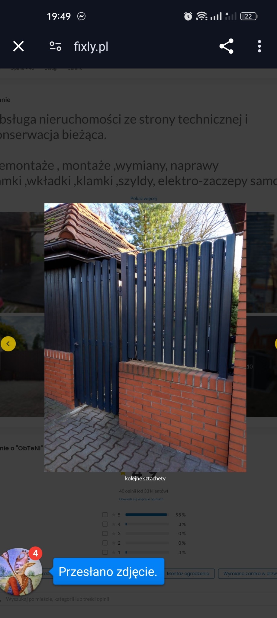 Nowoczesne ogrodzenie panelowe w kolorze grafitowym, zamontowane na niskiej, ceglanej podmurówce, z widoczną furtką i fragmentem elewacji budynku w tle.