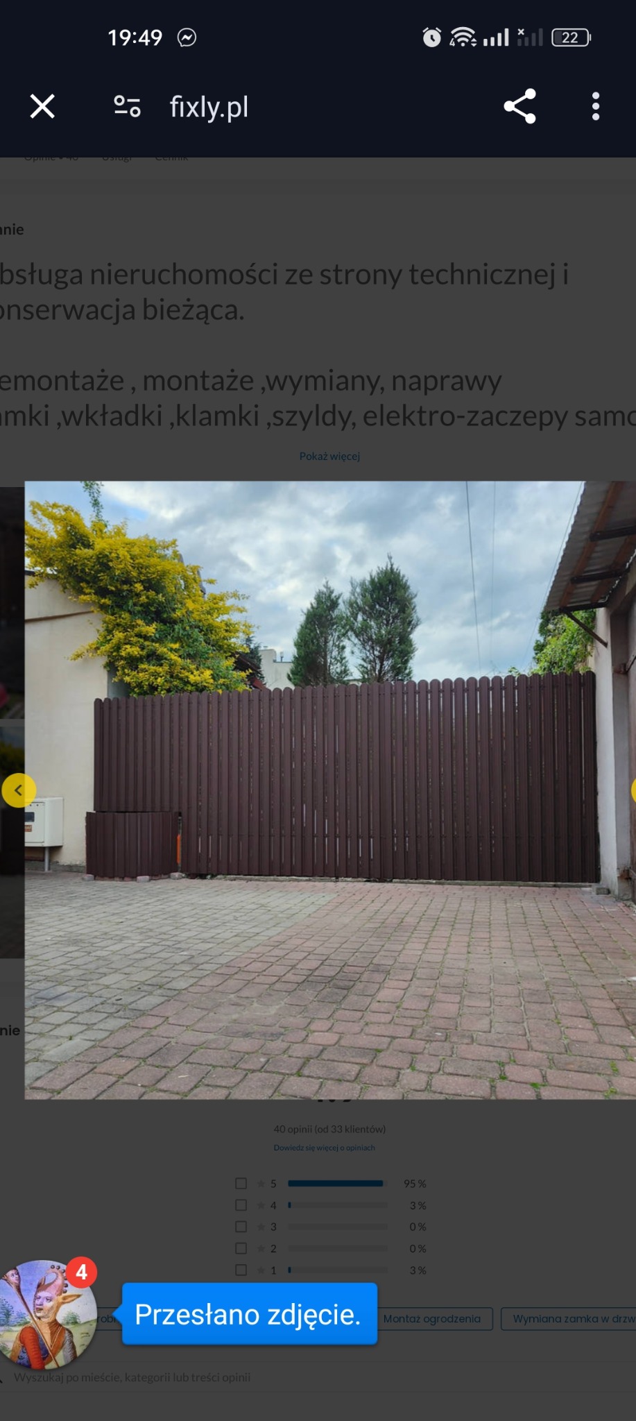 Ciemnobrązowe ogrodzenie panelowe z pionowych sztachet z dopasowanym pojemnikiem na śmieci, widok z zewnątrz na kostkę brukową.