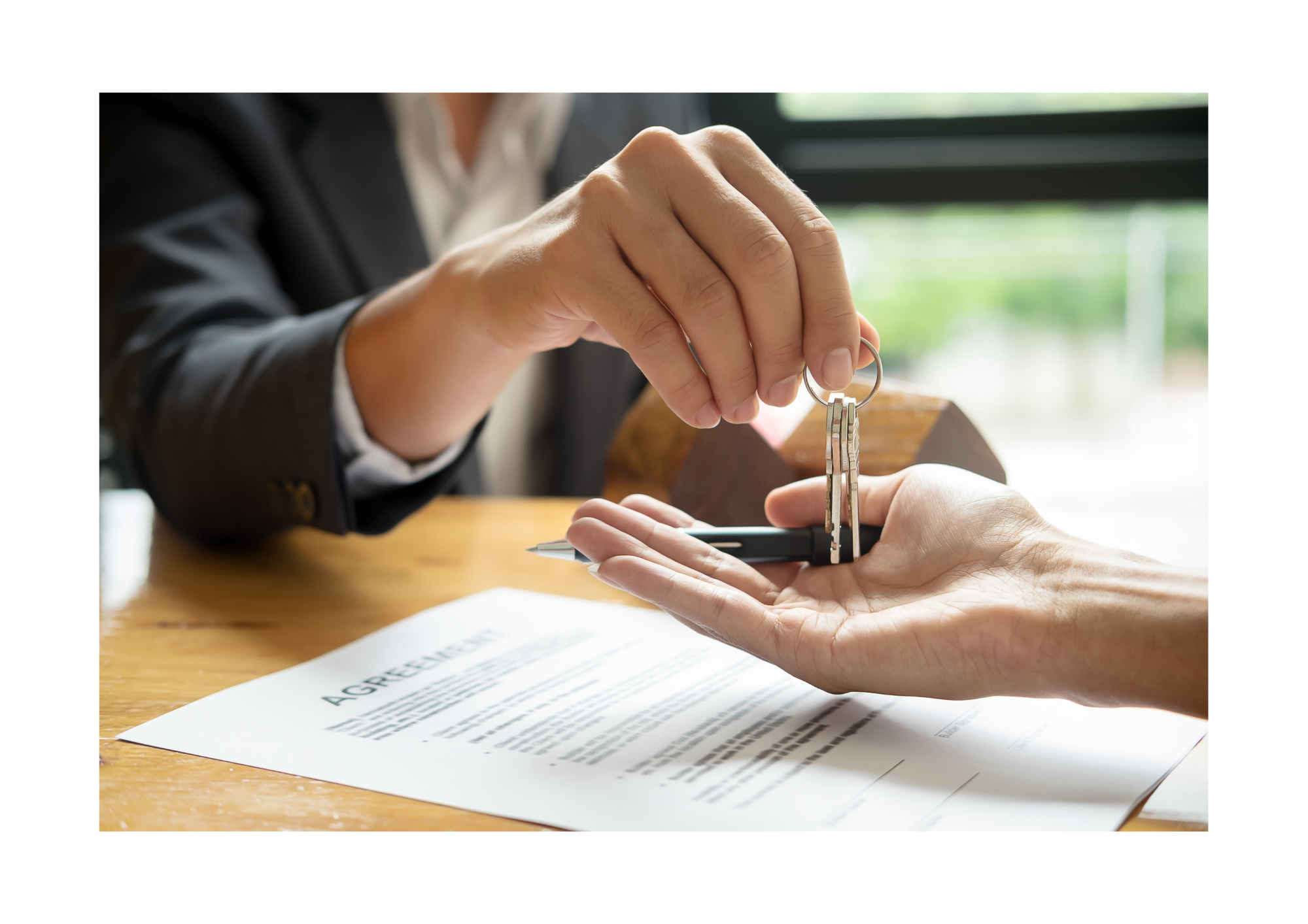 Przekazanie kluczy nad podpisaną umową, widoczny drewniany model domu w tle.