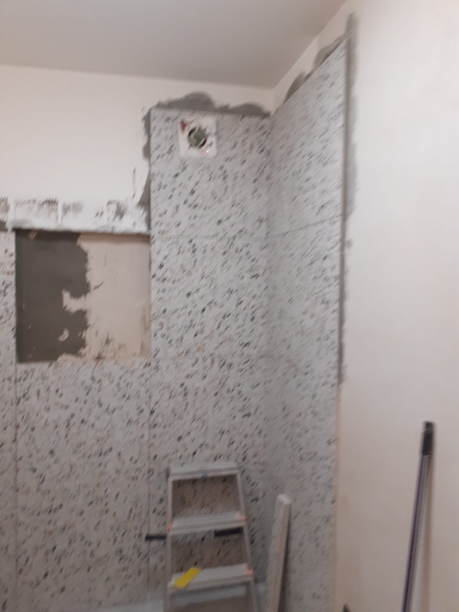 Montaż płytek lastryko w łazience, widoczny etap prac z drabinką i fragmentem ściany bez okładziny, przygotowanie pod wentylator.