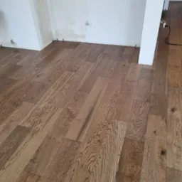 Ułożona drewniana podłoga w pokoju z niedokończonymi ścianami, widoczne kołki dystansowe przy ścianach.