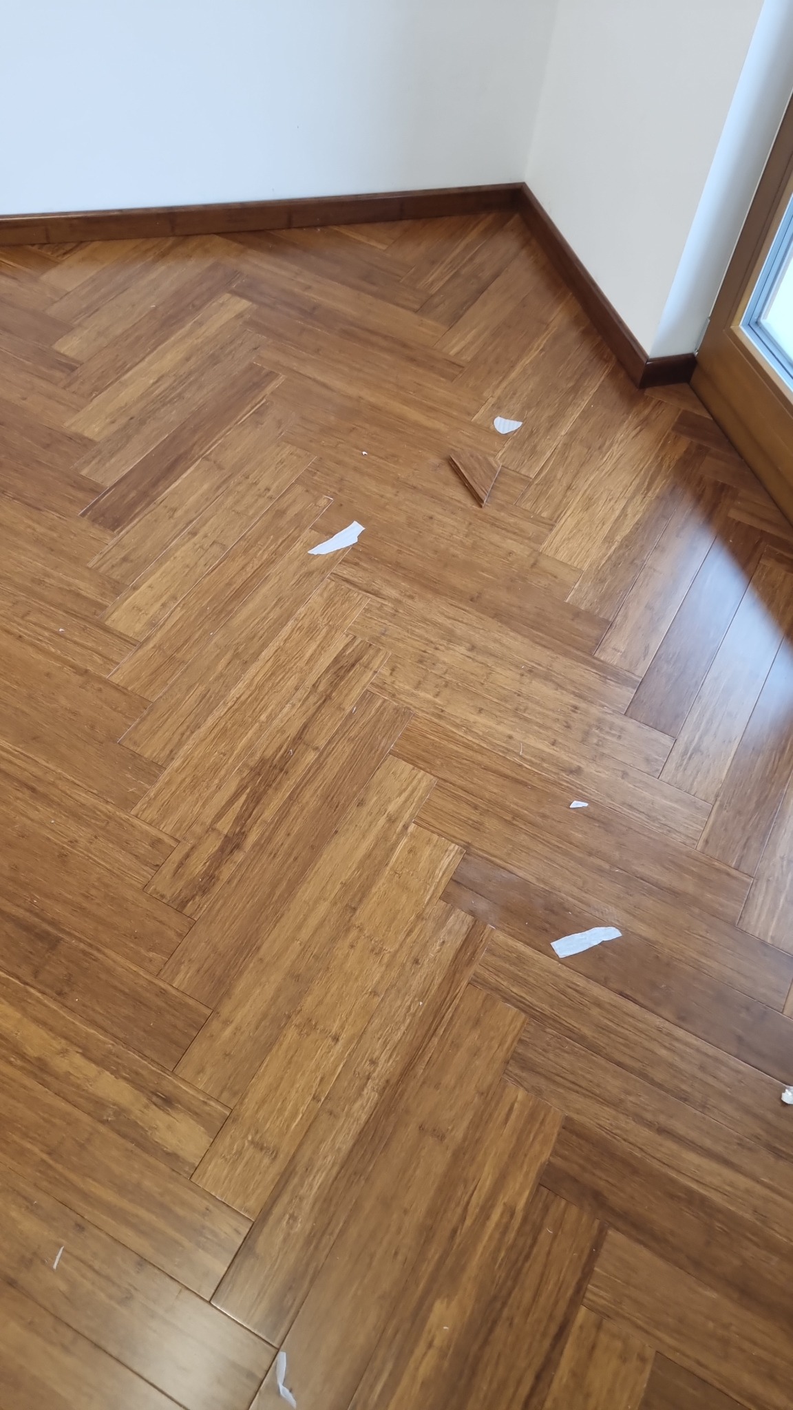 Ułożona podłoga z drewna w jodełkę, widoczne drobne ścinki i okleiny po montażu przy ścianie i oknie.